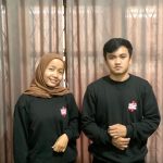 Sepasang pria dan wanita mengenakan sweater / kaos lengan panjang warna hitam polos dengan sablon logo kecil berwarna putih dan merah di dada kiri, berlatar belakang tirai cokelat. Kaos ini diproduksi oleh konveksi kaos jogja yang juga melayani kaos terdekat dengan kualitas sablon dan bordir jogja premium. Sempurna untuk konveksi baju komunitas.