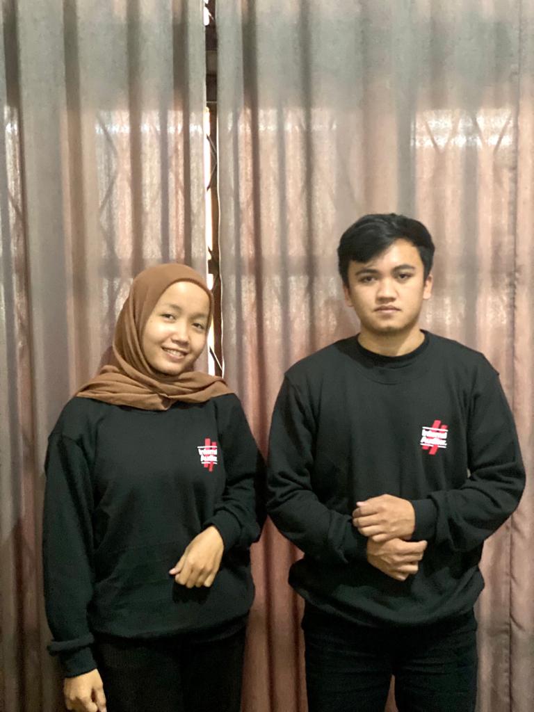 Sepasang pria dan wanita mengenakan sweater / kaos lengan panjang warna hitam polos dengan sablon logo kecil berwarna putih dan merah di dada kiri, berlatar belakang tirai cokelat. Kaos ini diproduksi oleh konveksi kaos jogja yang juga melayani kaos terdekat dengan kualitas sablon dan bordir jogja premium. Sempurna untuk konveksi baju komunitas.