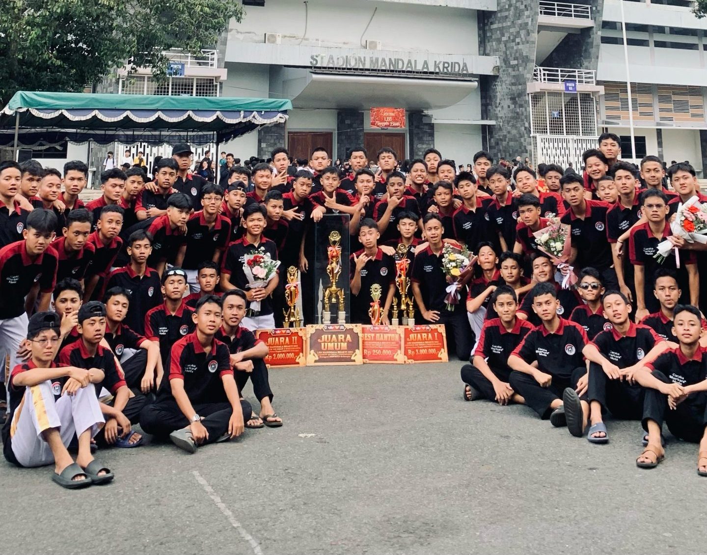 Kolase gambar menunjukkan kelompok besar pemuda/pelajar (mungkin tim olahraga/komunitas) mengenakan kaos polo shirt hitam dengan kerah merah, berpose merayakan kemenangan dengan piala dan penghargaan. Kaos polo ini sangat ideal untuk seragam event atau komunitas, diproduksi oleh konveksi kaos jogja yang ahli dalam bordir jogja presisi. Cocok untuk kebutuhan konveksi baju dan kaos terdekat berkualitas.